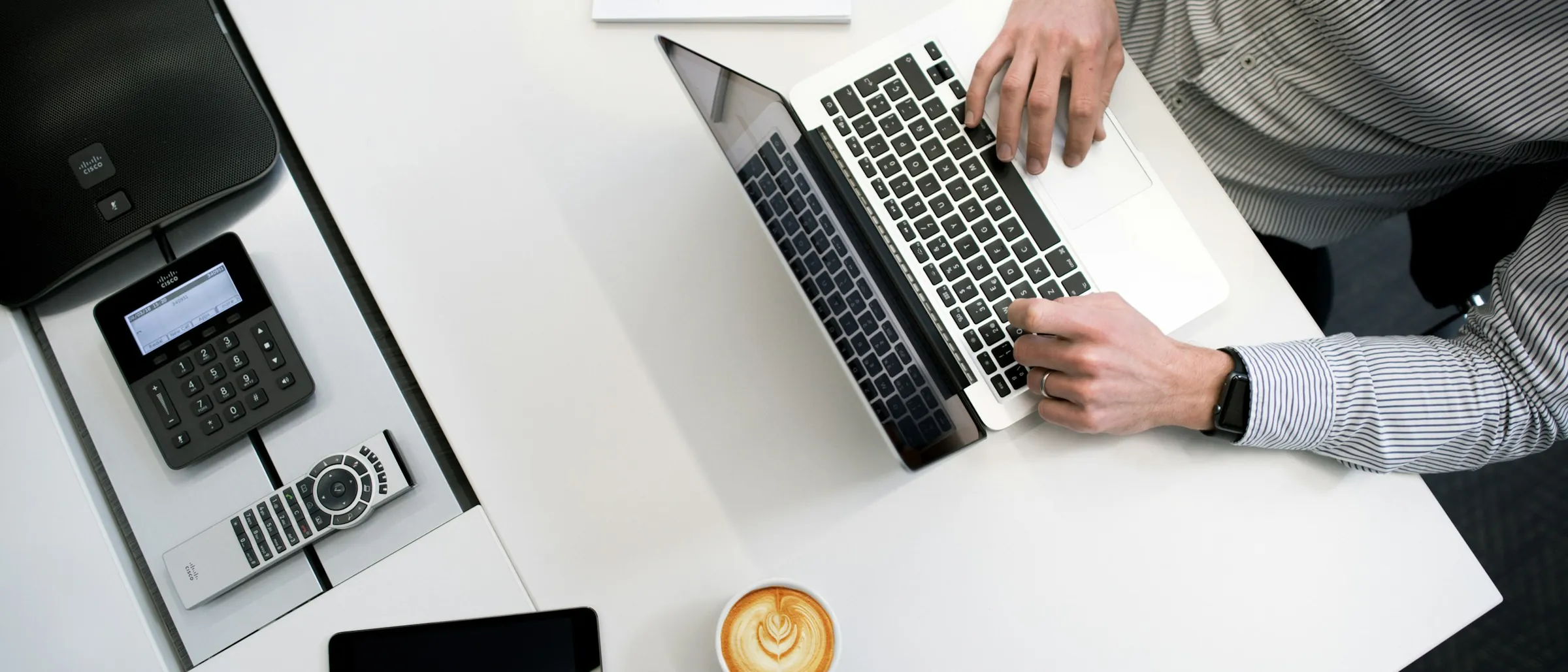 A laptop, phone and notepad on a clean white desk