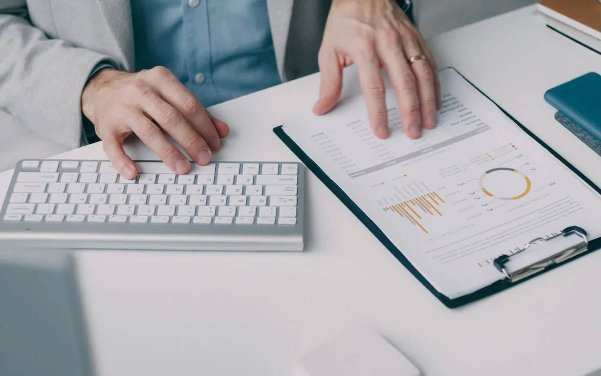 Hands on a keyboard beside a clipboard of printed reports
