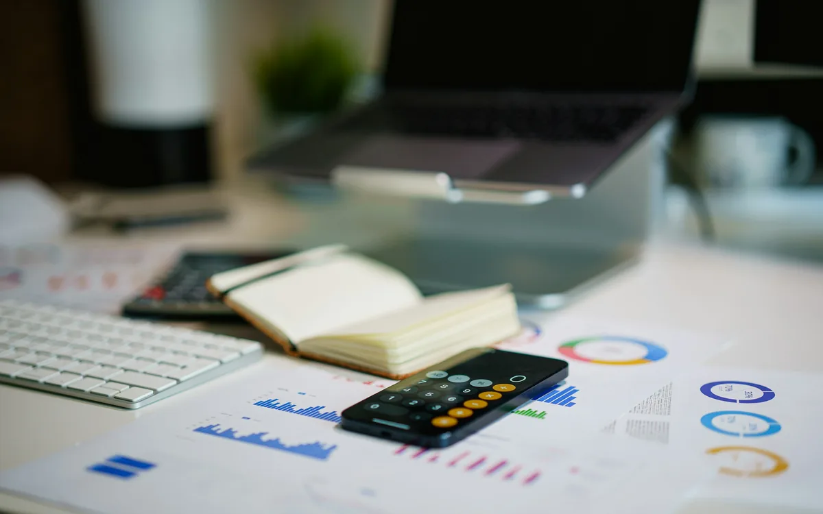 A desk of printed financial charts, a calculator and a notebook