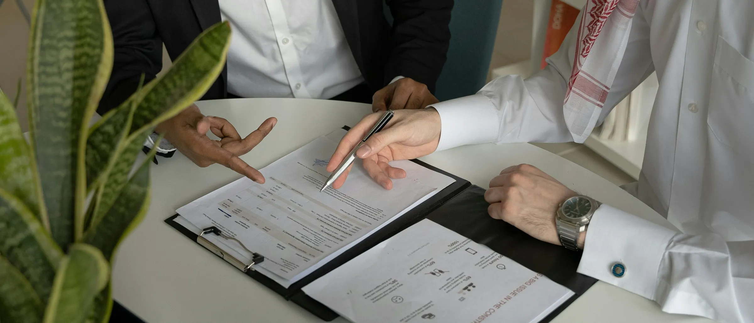 Two businessmen signing documents across a desk, one in traditional Emirati dress